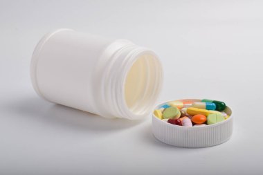 Beyaz arka planda izole edilmiş çeşitli hap ve kapsüllerle beyaz plastik ilaç şişesi açılmış. Sağlık ve eczane konsepti.