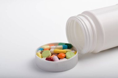 Beyaz arka planda izole edilmiş çeşitli hap ve kapsüllerle beyaz plastik ilaç şişesi açılmış. Sağlık ve eczane konsepti.