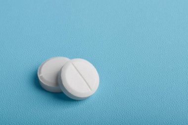 Mavi arkaplanda izole edilmiş iki beyaz tablet hap.
