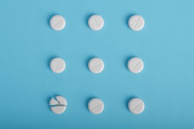 Mavi arka planda bir kareye yerleştirilmiş beyaz haplar, uyuşturucu dozajı ve ilaç kavramlarını tasvir etmektedir.