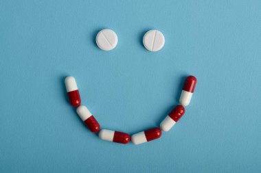 Mavi arka planda gülen surat şeklinde beyaz haplar tedavinin olumlu etkilerini sembolize ediyor..