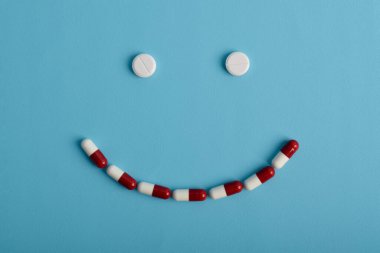 Mavi arka planda gülen surat şeklinde beyaz haplar tedavinin olumlu etkilerini sembolize ediyor..