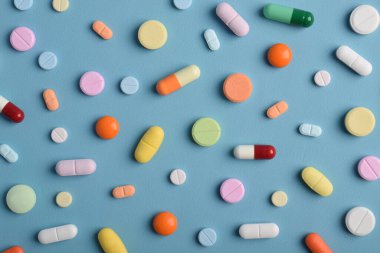 Mavi arka planda renkli hapların, tabletlerin ve kapsüllerin yakın çekimleri, sağlık, eczane ve tıbbi tedavi kavramları için çeşitli ilaçlar ve takviyeleri göstermektedir..