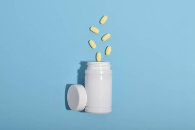 Açık ilaç şişesi mavi arka plana hap döküyor. Eczane, ilaç, vitamin, gıda takviyesi kavramı. Üst görünüm, metin için boş alan