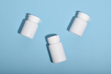 Mavi arka planda üç beyaz ilaç şişesi, eczane konsepti, sağlık ürünleri ve tıbbi malzemeler.