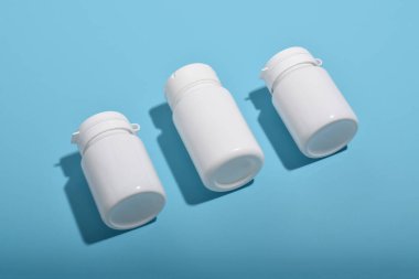 Mavi arka planda üç beyaz ilaç şişesi, eczane konsepti, sağlık ürünleri ve tıbbi malzemeler.