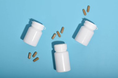 Three white medicine bottles and pills capsules on blue background, concept of pharmacy, healthcare products and medical supplies.