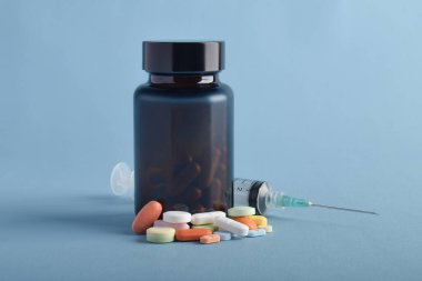 İlaç şişesi ve iğne mavi arka planda izole edilmiş. Tıbbi tedavi ekipmanları konsepti.