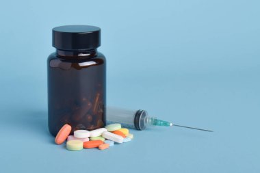 İlaç şişesi ve iğne mavi arka planda izole edilmiş. Tıbbi tedavi ekipmanları konsepti.