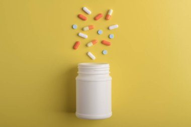 Sarı arka planda ilaç şişesinden çeşitli haplar ve kapsüller dökülüyor. Tıbbi konsept.