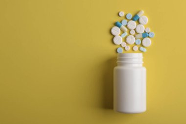 Sarı arkaplandaki ilaç şişesinden dökülen çeşitli haplar, üst görünüm, metin için kopyalama alanı. Tıbbi konsept.