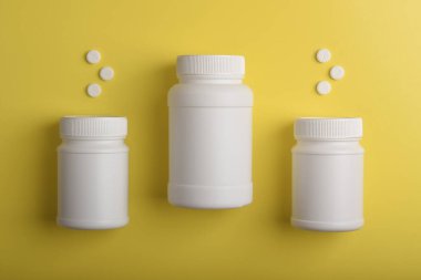 Sarı arka planda üç beyaz ilaç şişesi ve hap, eczane, sağlık ürünleri ve tıbbi malzemeler kavramı.