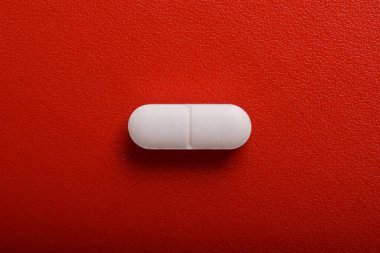 Kırmızı arka planda beyaz ilaç hapı. Üst manzara, düz uzanma.