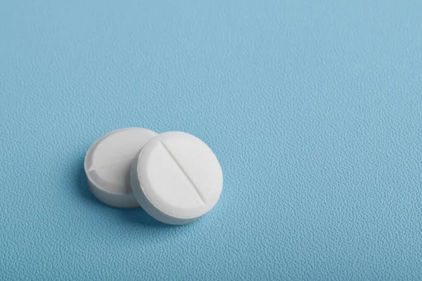 Mavi arkaplanda izole edilmiş iki beyaz tablet hap.