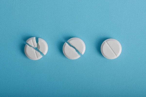 Beyaz yuvarlak tabletler mavi arka planda sıralanmış farklı kırık aşamalarda, ilaç dozajını, bölünmeyi ve ilaç kavramlarını gösteren.