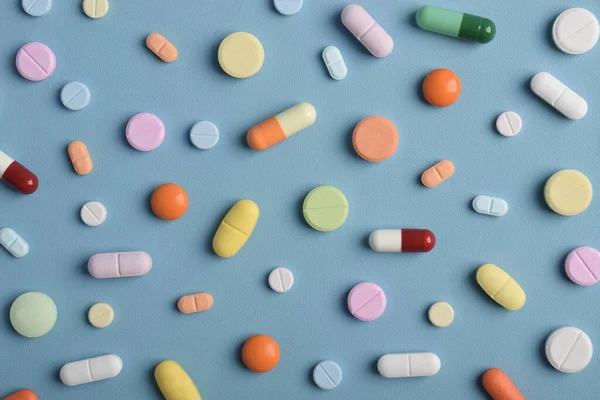 Mavi arka planda renkli hapların, tabletlerin ve kapsüllerin yakın çekimleri, sağlık, eczane ve tıbbi tedavi kavramları için çeşitli ilaçlar ve takviyeleri göstermektedir..