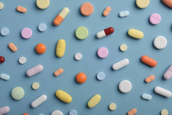 Mavi arka planda renkli hapların, tabletlerin ve kapsüllerin yakın çekimleri, sağlık, eczane ve tıbbi tedavi kavramları için çeşitli ilaçlar ve takviyeleri göstermektedir..