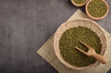 Ahşap kaselerde Mung fasulyeleri ve koyu taştan arka planda kepçeyle örülmüş sepet, kopyalama alanı, üst görünüm