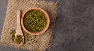 Mung fasulyeleri ahşap kasede. Çuval bezinde kaşık. Koyu taş arka planda..
