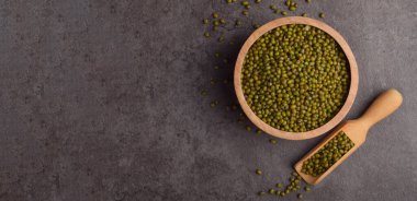 Ahşap kasede çiğ fasulye. Koyu taş arka planda kepçeyle. Üst manzara.