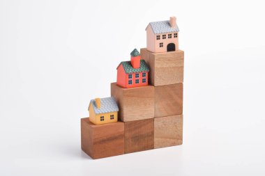 İstiflenmiş ahşap bloklara yerleştirilen minyatür evler yükselen emlak değerlerini, emlak yatırımlarındaki büyümeyi, konut piyasası eğilimlerini ve konut geliştirme kavramını temsil eden bir büyüme tablosu oluşturmaktadır..