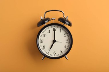 Saat yedide turuncu arka planda izole edilmiş klasik siyah alarm saati.