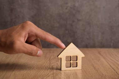 Minyatür bir evi işaret eden bir adam. Emlak kararları, uygun fiyatlı konutlar, emlak satın alma, satış, kiralama ve konut giderleri gibi konut giderleri, örneğin vergiler, kamu hizmetleri ve sigorta.