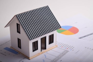 Mali tablolarda ve raporlarda minyatür bir ev. Emlak yatırım analizi, konut piyasası eğilimleri, gayrimenkul değer değerlendirmesi ve emlak yatırımı için stratejik planlama.