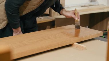 Zanaatkar atölyedeki ahşap yüzeye vernik uygular, zanaat ve hassasiyeti vurgular, kamera aksiyonu pürüzsüz doli hareketle takip eder
