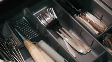 Mutfak gereçleri çekmecesinde çeşitli aletler yer almakta, kumaş ve malzemelerin vurgulanması için kademeli olarak yakınlaştırılmakta ve son olarak da çatal bıçak takımına uzanan bir el kullanılmaktadır.