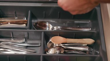 Çeşitli çatal bıçaklarla dolu bir çekmecedeki tahta saplı kaşığa uzanır. Organizasyon, doku, kamera tavaları ve netlik için yakınlaşır.