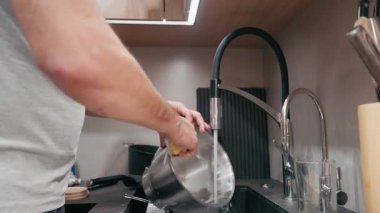 Çağdaş bir mutfakta bulaşık yıkayan erkek figürü, temizlik sürecini süngerle vurguluyor, sahne dokularını ve malzemelerini renklendiriyor