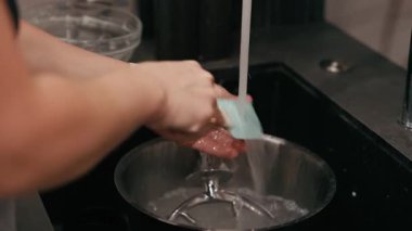 Ellerin yakın plan çekimleri fırın araçlarını ve kaseleri yıkamak, dokuları vurgulamak ve ekşi hamur pişirme sanatının sanatsal sürecini akıcı bir şekilde takip etmek.