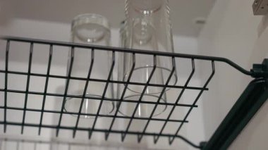 Kamera yaklaştıkça, modern bir mutfak ortamında şeffaflık ve zarif tasarımlarını vurgulayarak tel raftaki bardaklar vurgulanıyor.