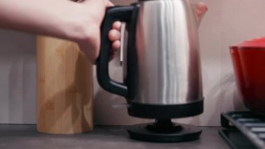 Paslanmaz çelik çaydanlık, yakınlarda bambu tutacağı ve kırmızı tencereyle, mutfak işlevini ve tasarımını ön plana çıkaran bir el tarafından çalıştırılıyor.