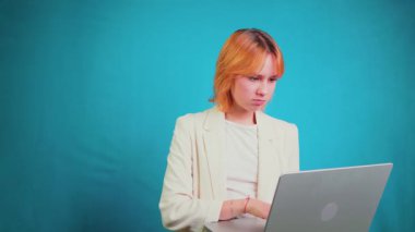 Sinirli genç iş kadını dizüstü bilgisayarı üzerinde çalışırken stresli hissediyor, bilgisayar sisteminde sorunlar yaşıyor, katı mavi arka planda hayal kırıklığı ve kafa karışıklığı gösteriyor