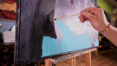 Profesyonel erkek sanatçı, stüdyo atölyesinde bir fırçayla soyut bir resim çiziyor. Turkuaz tuval üzerinde siyah akrilik kullanarak çağdaş bir sanat eseri yaratma süreci