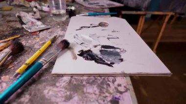 Bir başyapıt yaratmak için gerekli araçlara sahip yaratıcı resim atölyesi. Profesyonel ahşap palet, karışık siyah-beyaz yağlı boya boya, fırça ve tüpler ile dağınık, boya sıçramış bir masa.