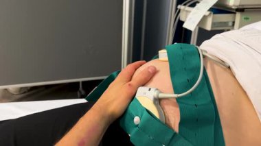 Erkekler, fetal kalp atış hızı ve kasılma izleme prosedürü sırasında hamile eşlerinin karnını nazikçe okşayarak bebeklerini beklerken konfor ve destek sağlıyorlar.