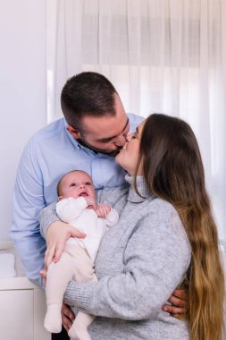 Mutlu ebeveynler bebeklerini kucaklar ve şefkat gösterirler. Yeni hayatı, aile bağlarını ve ebeveynliğin neşesini sembolize ederler. Parlak, samimi bir ortamda.