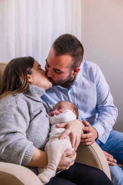 Sevgi dolu ebeveynler şefkatli bir öpücüğü paylaşıyorlar, yeni doğan bebeklerini tutarken sevgilerini ifade ediyorlar, aile bağlarını, yeni ebeveynliği ve ilgiyi simgeliyorlar.