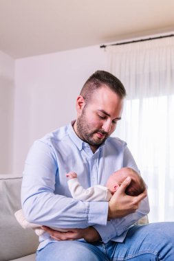 Yeni baba, yeni doğmuş bebeğini nazikçe kucaklıyor. Küçük oğluyla samimi bir anne-baba ve aile bağı kuruyor. Evlerinin parlak ışığında.