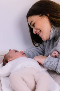 Genç anne yeni doğmuş bebeğiyle bağ kuruyor. İkisi de derin anne sevgisini ve aile bağlarını yansıtırken başını nazikçe tutuyor.