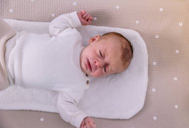 Yeni doğmuş bebek gözleri kapalı ve ağzı açık ağlar, beyaz benekli bej bir waffle battaniyesinde uzanır, üzgün hisseder ve üst perspektiften rahatsız olur.