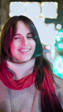 Neşeli genç bir kadın, neşeli bir akşamın tadını çıkarıyor. Tatillerde şehrin parlak ışıkları önünde gülümsüyor ve gülüyor. Kış atmosferinde otantik neşe ve mutlulukla dolu.