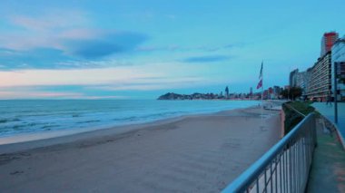 Benidorm, İspanya 'daki gezinti güvertesinden deniz manzaralı güzel bir gün doğumu manzarası. İnsanlar arka planda şehrin ufuk çizgisi olan boş rıhtımda yürüyor ve egzersiz yapıyor.