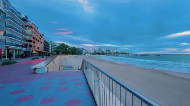 Benidorm, İspanya 'daki ikonik levante plajının güzel panoramik manzarası, sakin mavi bir akşamda sakin dalgalar kumlara yuvarlanırken liman boyunca şehir binaları.