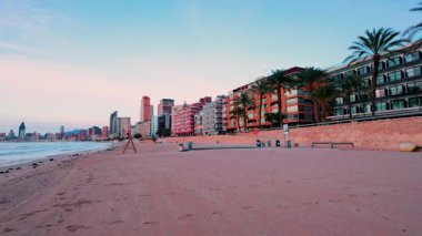 Benidorm, İspanya 'daki boş levante kumsalının manzarası şehrin ufuk çizgisini, sakin Akdeniz' i ve renkli ve sakin günbatımında ikonik benidorm adasını gözler önüne seriyor.