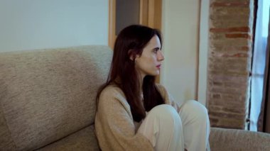Depresyonda olan yalnız bir genç kadın kanepede oturup pencereden dışarı bakıyor. Düşünceli ve endişeli bir kadın. Terk edilmiş ve üzgün. Evde akıl sağlığı sorunları yaşıyor.