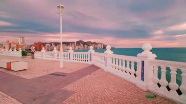 Benidorm, İspanya 'daki Akdeniz manzaralı balkonun beyaz balkonunda, renkli ve dramatik bir günbatımında levante plajı ve şehir siluetini gösteren görüntüler.